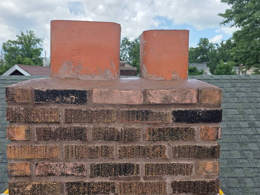 The same chimney rebuilt, with clean new brick courses, a level crown and two clay flue tiles standing proud against a blue sky.