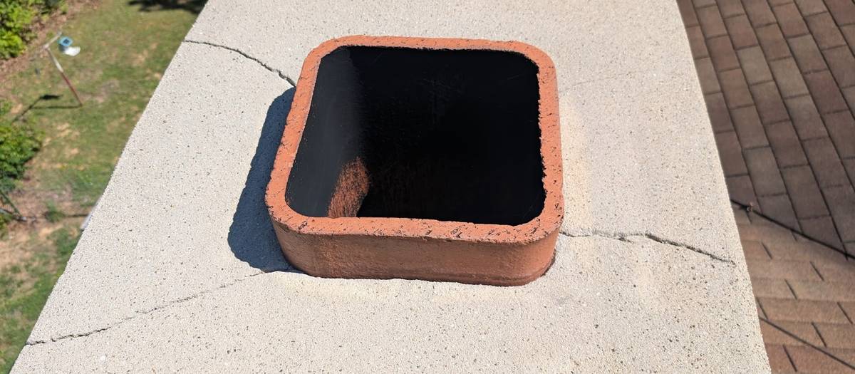 A top-down view of a chimney crown with a rectangular clay flue tile standing in the middle and a hairline crack running across the crown.